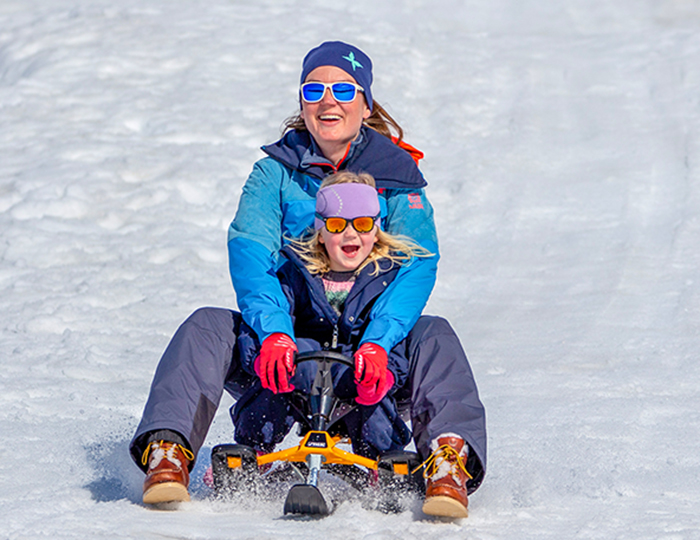 A family enjoying skiing together in Beitostølen, Valdres, Norway. A child learns to ski, while others glide smoothly over the snow. A quaint chalet blends into the picturesque winter sports scene.