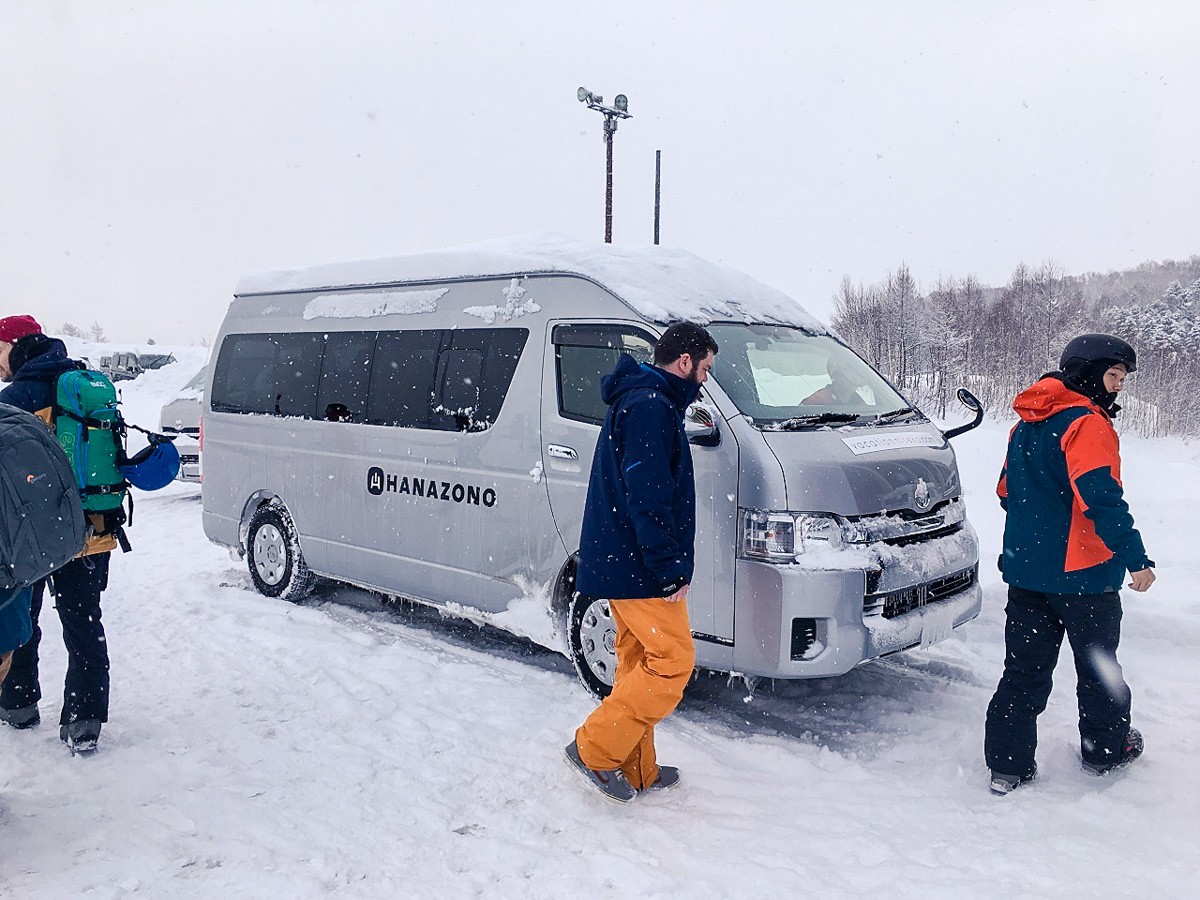 Niseko Weiss Cat in Japan - a group of people standing around a van in the snow.