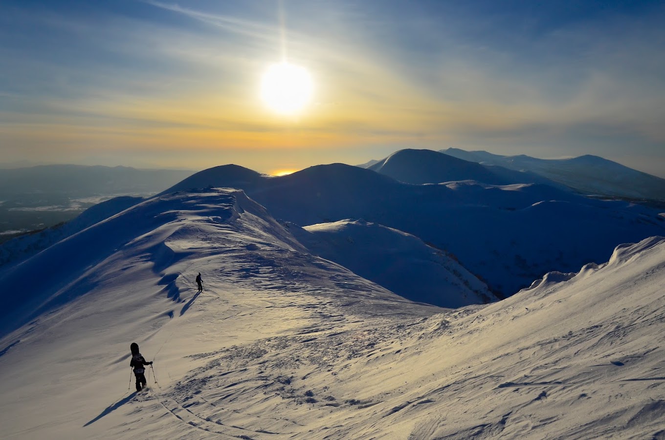 A skier and a snowboarder making their way down the snowy slopes of Niseko Weiss Cat in Kutchan, Abuta District, Hokkaido, Japan. The stunning winter landscape and mountain in the background enhance the beauty of the scene.