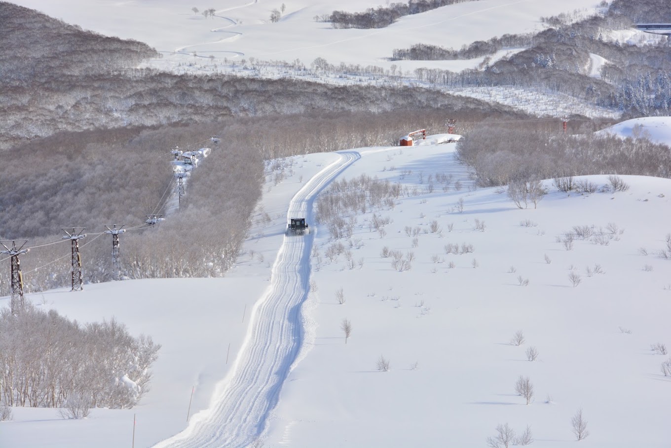 Skier glides across a winter sports scene at Niseko Weiss Cat in Kutchan, Hokkaido, surrounded by a stunning winter landscape. A snowmobile waits nearby at this popular ski resort.
