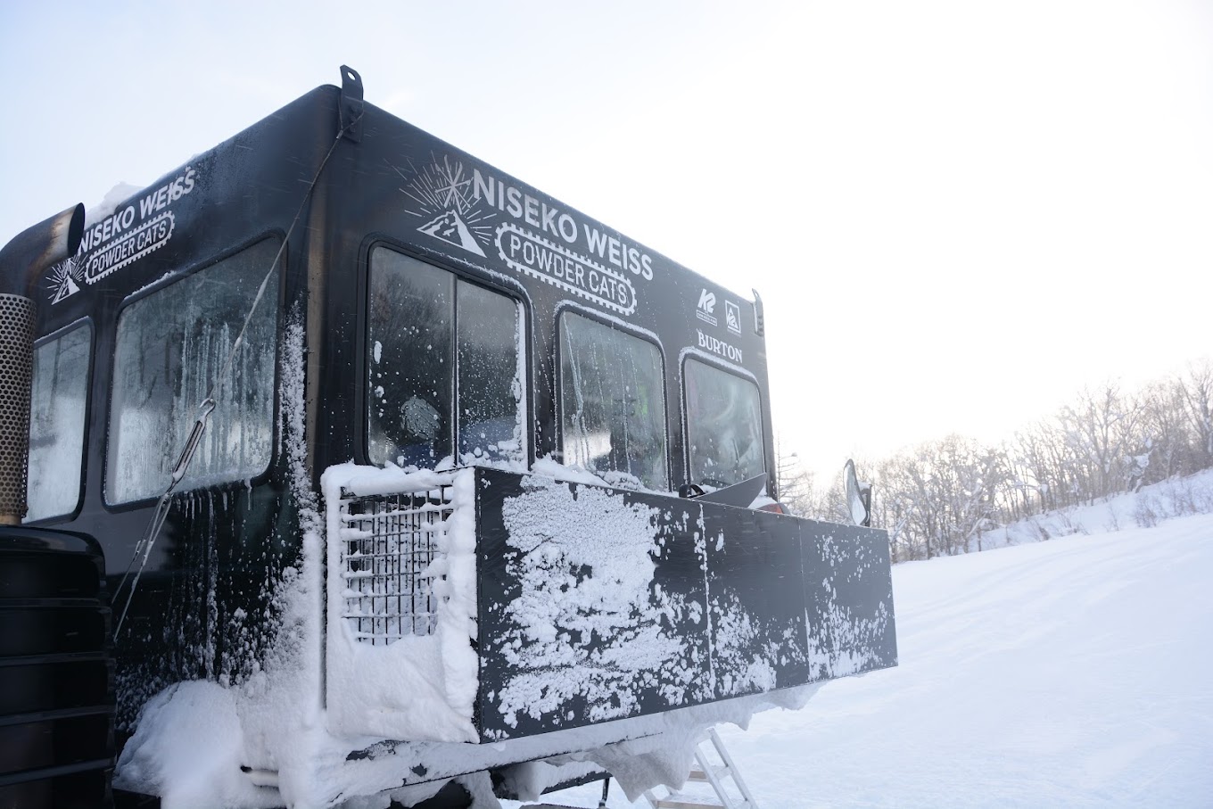 Winter scene at Niseko Weiss Cat in Japan featuring stunning snow-covered landscape, a snowmobile, with activities at a winter sports center in the backdrop.