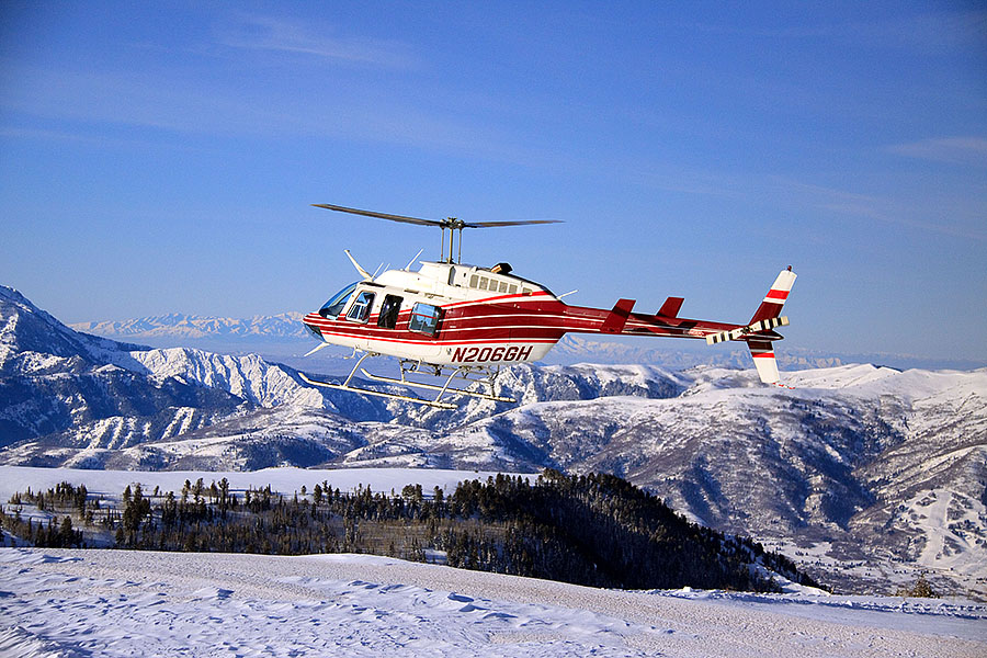 View of Diamond Peaks in Utah during winter featuring a bustling ski resort with a snowmobile driving past skiers on a snow-covered slope and a ski lift in the background.