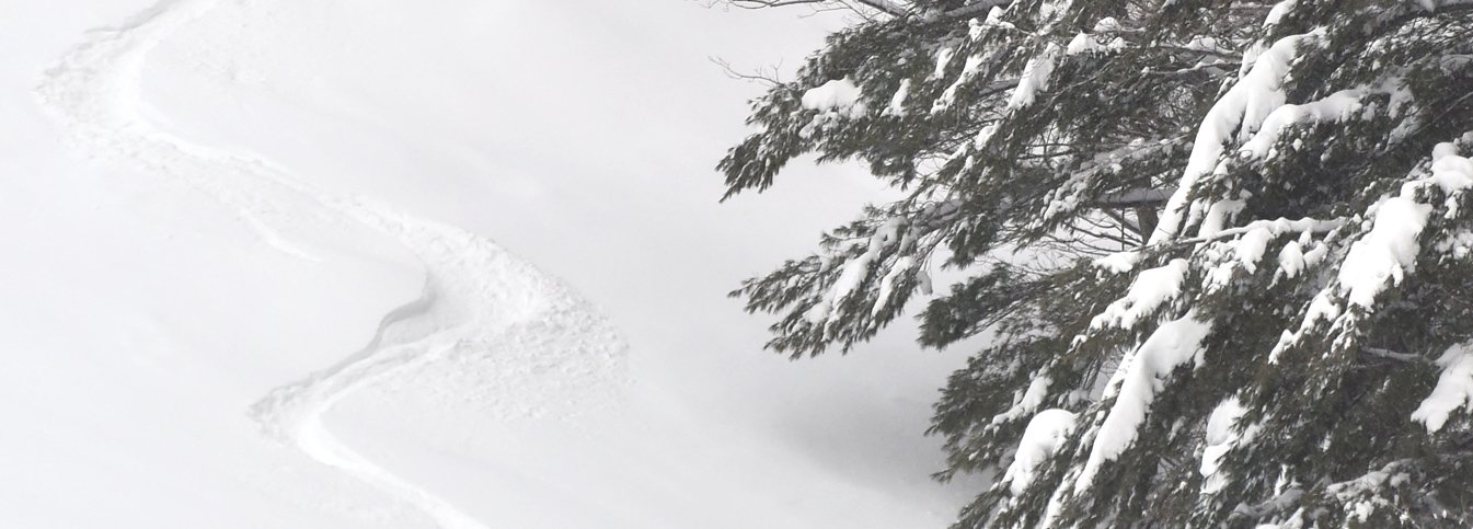 A skier navigates down the snowy slopes of Mad River Glen in Vermont, with a snowmobile and chalet nearby, creating a quintessential winter sports scene at a ski resort.