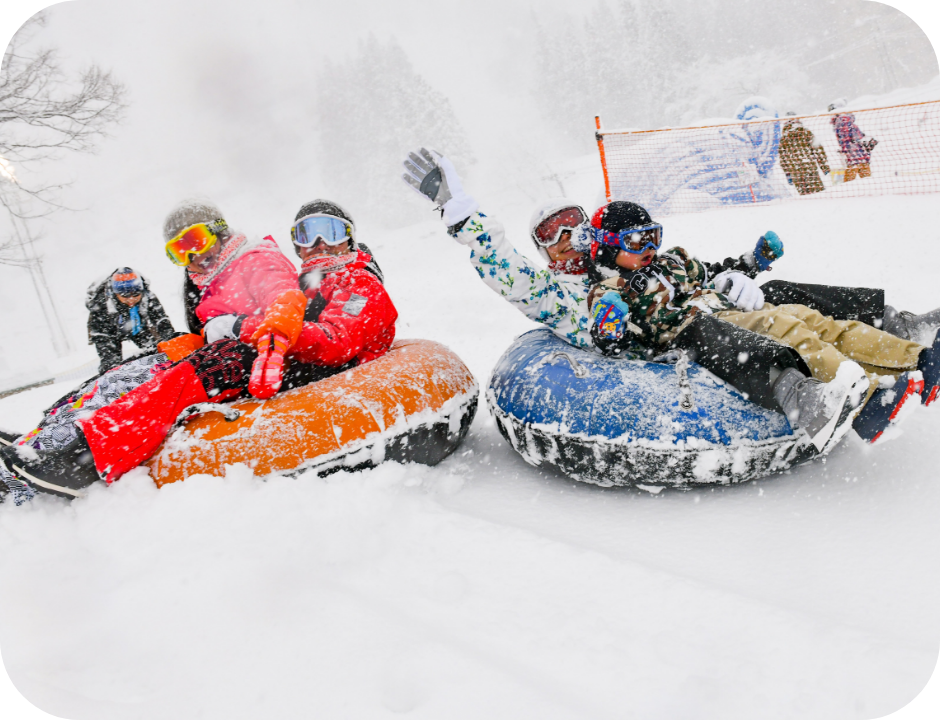 Winter sports scene in Chūbu, Japan, featuring a snowmobile amidst a group of people and families enjoying skiing at the Yuzawa Kogen | ​Gala Yuzawa | ​Ishiuchi Maruyama ski resort.