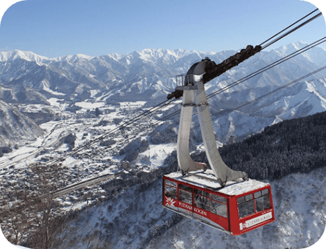 Ski lift ascending a snowy slope in the popular ski resort Yuzawa Kogen, Gala Yuzawa, Ishiuchi Maruyama in Chūbu, Japan. A skier can be seen near a challet in this winter sports scene.