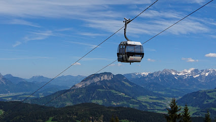 Austrian ski resort at Ski Juwel Alpbachtal Wildschönau - Markbachjochbahn, showcasing a ski lift moving near a charming chalet, with a skier and majestic mountain in the backdrop.