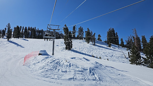 A winter sports scene at China Peak Mountain Resort in Lakeshore California featuring a skier on a ski lift overlooking the snowy ski resort.