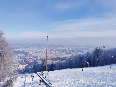 Winter scene at Mariborsko Pohorje in Slovenia featuring a bustling winter sports scene amidst stunning snow-covered surroundings. A charming chalet is visible, adding to the ambiance of the winter sports centre.
