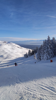 Skier making their way down snow-covered slopes at Monts Jura ski resort in Lélex, France. A charming challet is visible near the base of the winter sports scene.