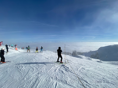 Skier making a descent on a snowy slope at Monts Jura - Station Crozet - Lelex in France. The scene is dotted with other skiers and chalets, showcasing a lively winter sports scene at the ski resort.