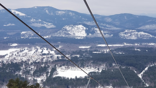 A picturesque view of Cranmore Mountain Resort featuring a busy ski lift carrying winter sports enthusiasts up the frost-coated slopes. Skiers are enjoying the well-groomed trails against the backdrop of a welcoming chalet.