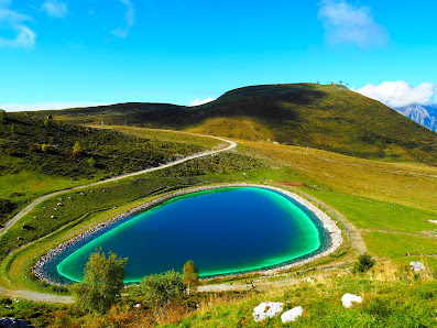 View of the serene lake in Piani di Bobbio, Val Brembana, with a charming chalet nearby. Snow-capped mountains and a winter sports center mark the background in this idyllic Italian landscape.