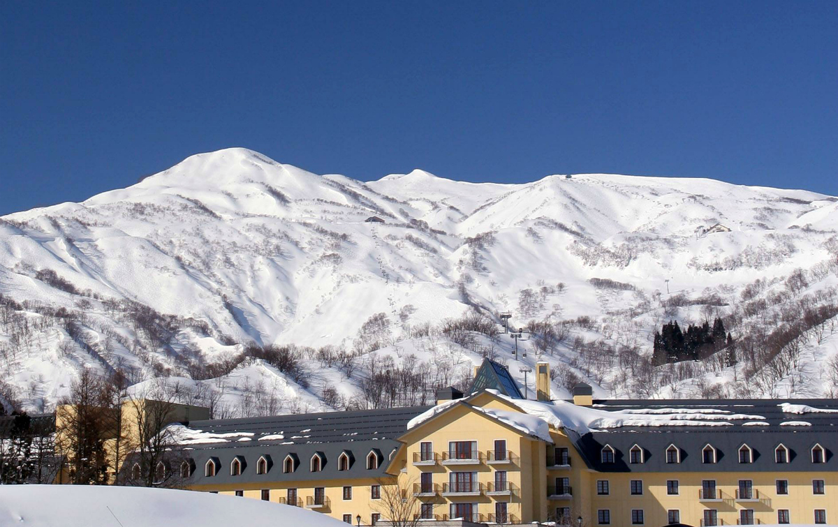 Lotte Arai Resort in Japan - a yellow house in the snow with mountains behind.