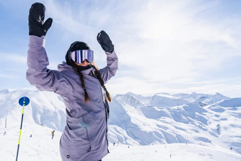 A skier and snowboarder enjoying a sunny winter day on the slopes of Astún Ski Resort in Aragon Huesca Spain with a quaint chalet nestled in the background.