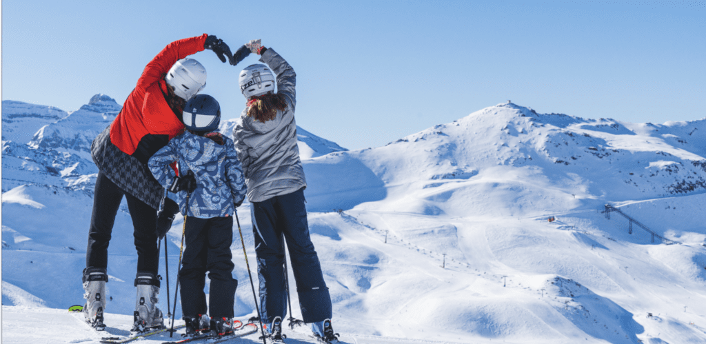 A lively scene at Astún ski resort in Aragon Spain. A family is enjoying skiing down the snow-covered slopes with a quaint chalet nestled in the background. The atmosphere is full of winter sports excitement.
