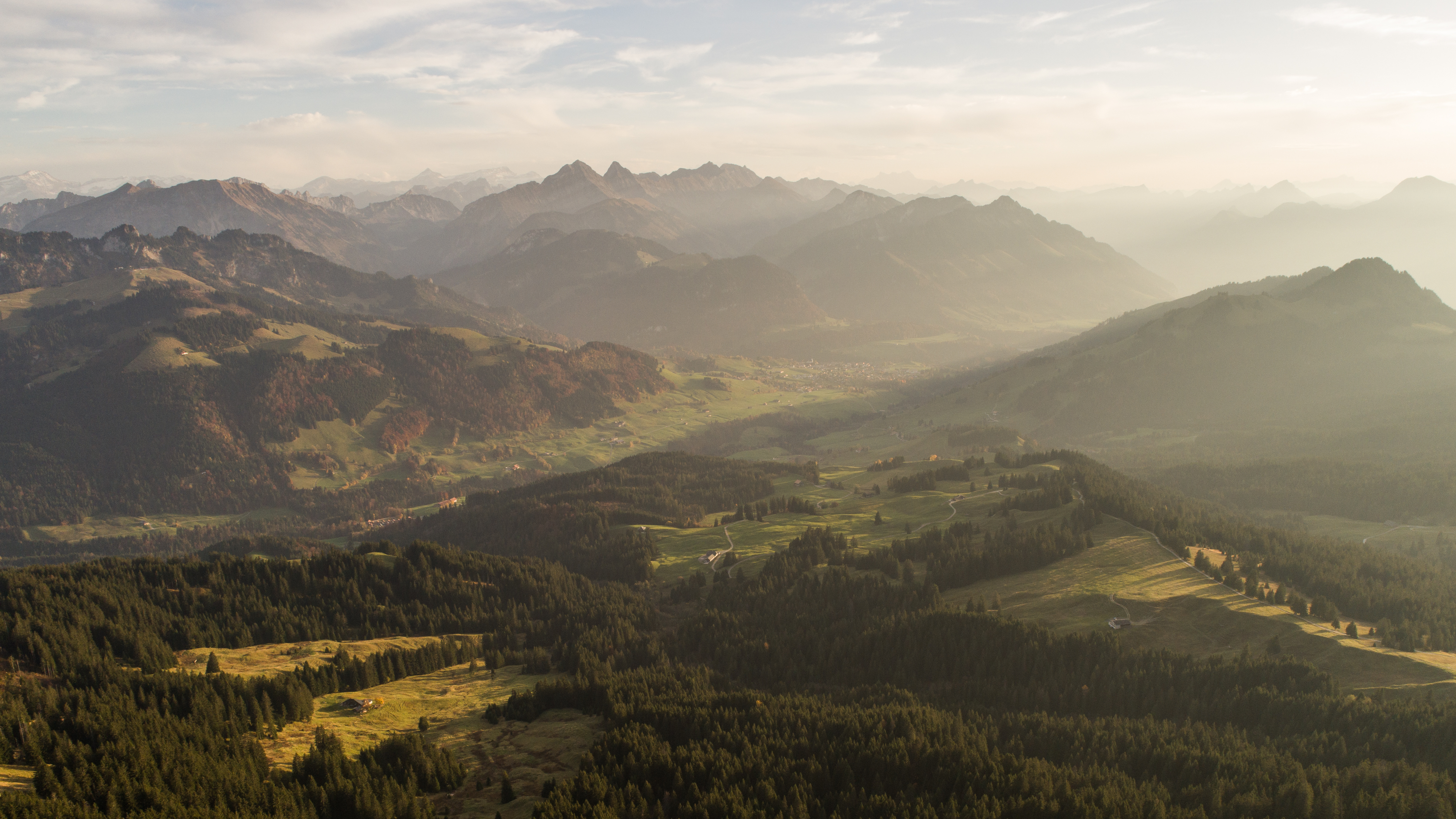A charming challet in La Berra, Switzerland sits amidst scenic mountain ranges on a sunny day. A mountain bike rests nearby, hinting at recreational activities in the area.