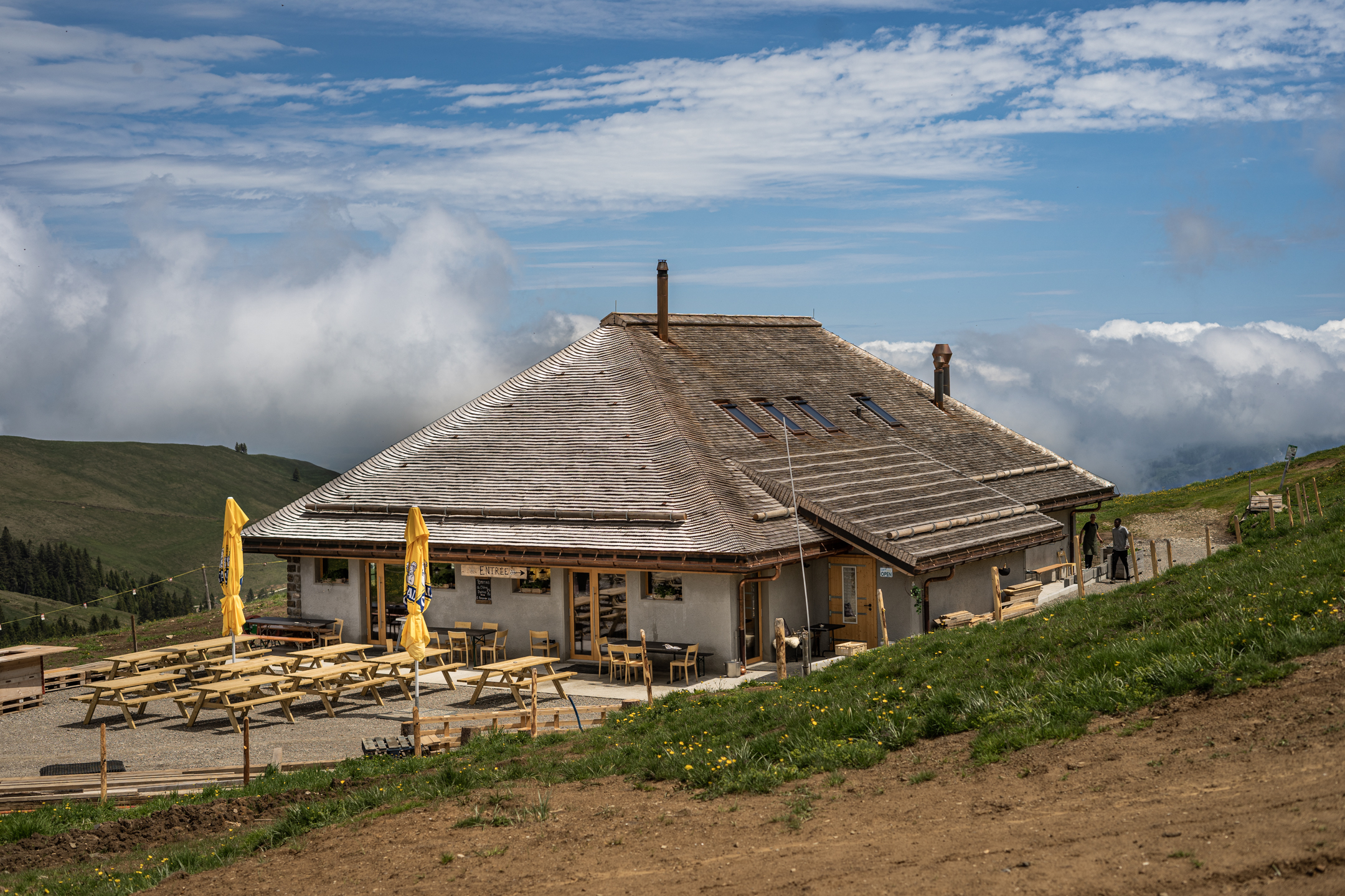 A charming mountain hut featuring aspects of a challet and lodge nestles peacefully in the stunning La Berra region of Switzerland surrounded by the majestic backdrop of a serene mountain and nearby ski resort.
