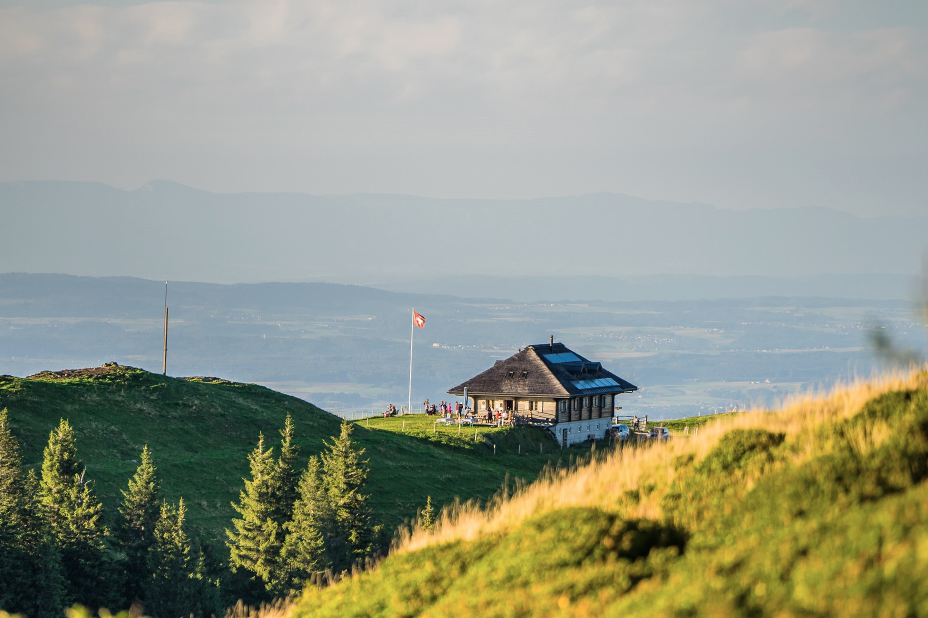 View of a charming mountain hut and a challet in La Berra, Switzerland, nestled among the majestic mountain range. A ski lift is faintly visible in the distance, completing this picturesque, alpine scene.