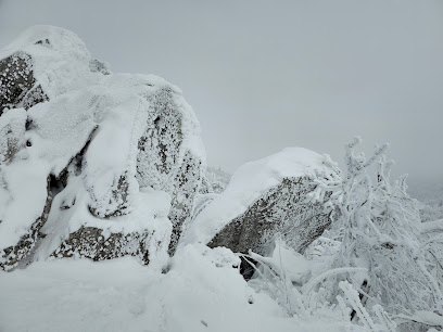 Skier descending a snowy mountain slope in Luchon Superbagnères, France, with a mountain hut and challet in the background, on a clear winter day.