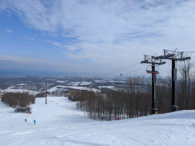 Winter scene at Blue Mountain Resort in The Blue Mountains, Ontario, showcasing busy ski slopes, a moving ski lift, skiers in action, and a cozy chalet nestled in the snow-covered landscape.