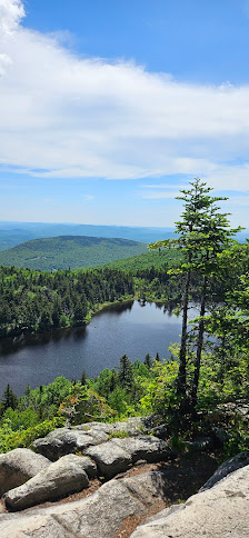 View of Mt Sunapee in Newbury, New Hampshire displays a serene lake surrounded by a lush forest. A charming challet nestles nearby. The mountain backdrop completes this sunlit, picturesque scene.