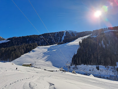 Winter scene at Nuova Carì in Valle Leventina, Switzerland, featuring a chalet and a bustling ski resort packed with sports enthusiasts. Visible are the ski lift and sports centre.