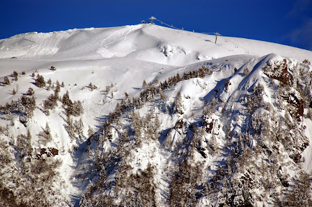 A skier gliding down snowy slopes at Montecampione Ski Area, surrounded by majestic mountains. A ski lift in the backdrop under a clear blue sky enhances the scenic beauty of Lombardy, Italy.