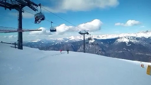 A skier descends a slope at the Montecampione Ski Area in Camonica Valley, Italy. The background features a ski lift and a snow-covered mountain. The atmosphere suggests lively winter sports activities.