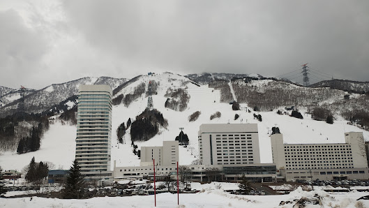 Scenic view of Naeba ski resort in Niigata, Japan, featuring stunning winter landscape, bustling winter sports activities and a ski lift traversing the resort.