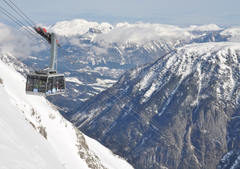 A picturesque view from Kitzbüheler Horn ski resort in Tyrol Austria showing a ski lift skier making their way down the slope and a cozy chalet nestled in the snowy landscape.