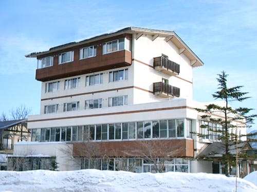 View of the picturesque Hakuba 47 | Goryu winter sports centre in Chūbu, Honshu, Japan with a cozy chalet and lodge nestled among snow-covered mountains, highlighting a bustling ski resort scene.