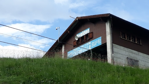 View of a charming Swiss chalet at Espace Dent Blanche, a ski resort in Télé Evolène, Valais. The lodge, situated amid snow-clad mountains, also features a glimpse of a ski lift.