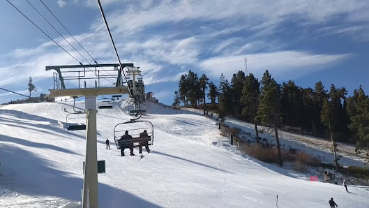 A skier enjoying winter sports at the Bear Mountain – Big Bear Lake, a ski resort in California with a ski lift in the background and a snowmobile in sight.