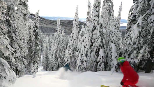 Winter scene at Baldy Mountain Resort in Oliver, British Columbia, showcasing a lively ski resort with a skier gliding down the mountain and a ski lift operating in the background.