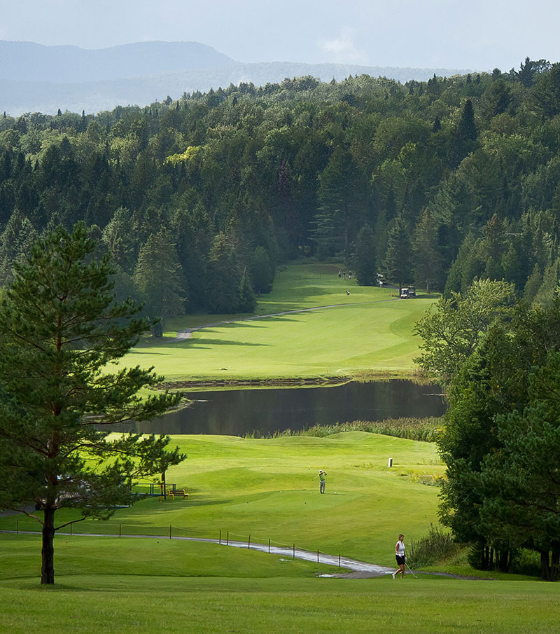 A chalet surrounded by a fresh snow scene at Owl's Head, with a winter sports scene visible in the distance. The ski resort is nestled amongst a forest of trees on the mountain.