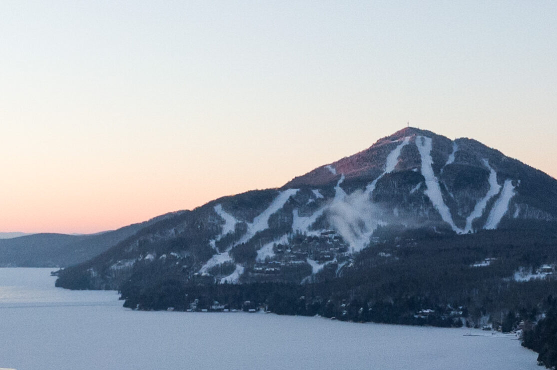 Overlooking the scenic Owl's Head mountain in Mansonville Quebec featuring a quaint ski resort a lone skier in motion on the snow-covered slopes exemplifying a vibrant winter sports scene.