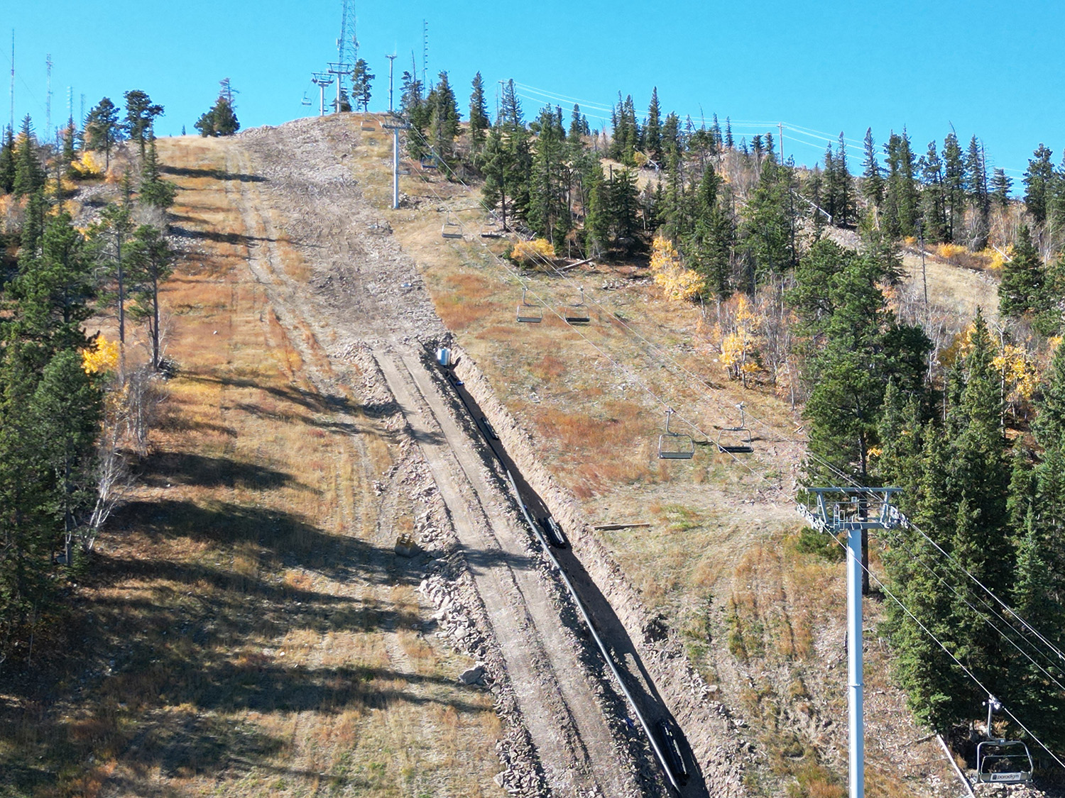 A ski lift is rising over Terry Peak in Lead South Dakota with a ski resort mountain and skier faintly visible.