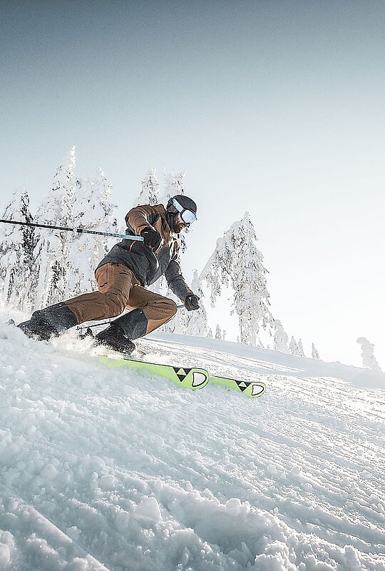 A skier enjoying a winter sports scene at Hochficht in Mühlviertel, Upper Austria. The skier gracefully navigates the snowy slopes, with a ski lift, a snowboarder, and a snowmobile visible in the tranquil scene.