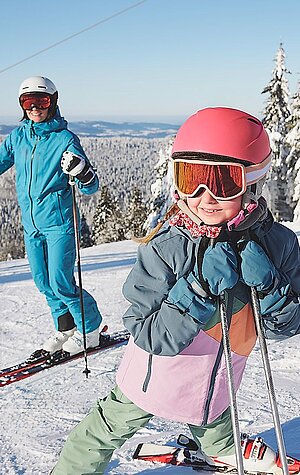 A skier and a snowboarder enjoy the winter sports scene on Hochficht mountain in Mühlviertel, Austria, with a family skiing nearby and a ski lift in the background.