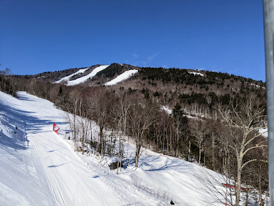 Winter sports scene at Waterville Valley Resort, New Hampshire, USA, featuring a skier on snow-covered slopes with a ski lift in the background.