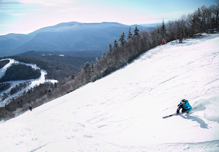 Winter sports enthusiast skiing downhill at Waterville Valley Resort, New Hampshire amidst a picturesque setting of snow-covered slopes. A ski lift is visible in the backdrop.