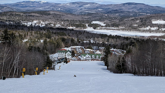 A scenic winter view at Ragged Mountain Danbury New Hampshire displaying a lively ski resort dotted with sport enthusiasts skiing down the snowy slopes. The landscape is adorned with ski lifts aiding the fun.