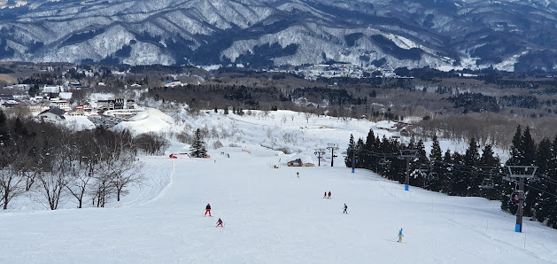A beautiful winter scene at Myoko Akakura Kanko ski resort in Honshu, Japan featuring scenic snow-covered slopes with crisp, white snow. Skiers elegantly navigate through the stunning landscape.