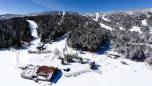 Scenic view of Collet ski resort in Allevard, France featuring snowy slopes, a rustic chalet, and lively winter sports activities under a clear blue sky.