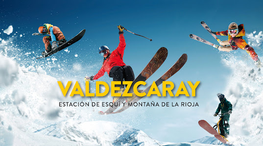 View of a chalet in Valdezcaray, Spain surrounded by a vibrant winter sports scene. Skiers and groups of people enjoy the snowy slopes at the busy winter sports centre.
