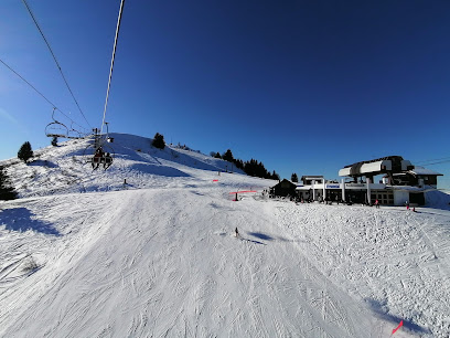 A breathtaking view of Château-d'Oex ski resort in Switzerland, displaying a vibrant winter sports scene. Surrounded by snow-covered mountains is a picturesque challet and a busy ski lift.