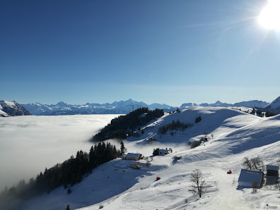 Sunny day at Station Brasses ski resort in Bogève, France, featuring a chalet, skiers enjoying winter sports on the mountain slopes of the majestic Mont Blanc.