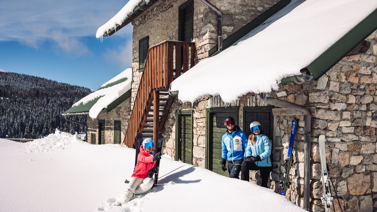 Alpe Cimbra | Folgaria in Italy: two people standing outside of a stone building in the snow.