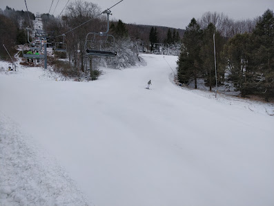 A skier glides down a slope at the Camelback Ski Resort in Tannersville Pennsylvania USA. In the background a ski lift carries more patrons uphill. The scene is a vision of winter sports enjoyment with a snowmobile nearby.