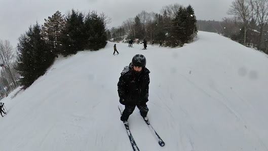 A skier is enjoying the snowy slopes at Camelback resort in Tannersville Pennsylvania. In the background there's a ski lift and other individuals engaging in winter sports activities.
